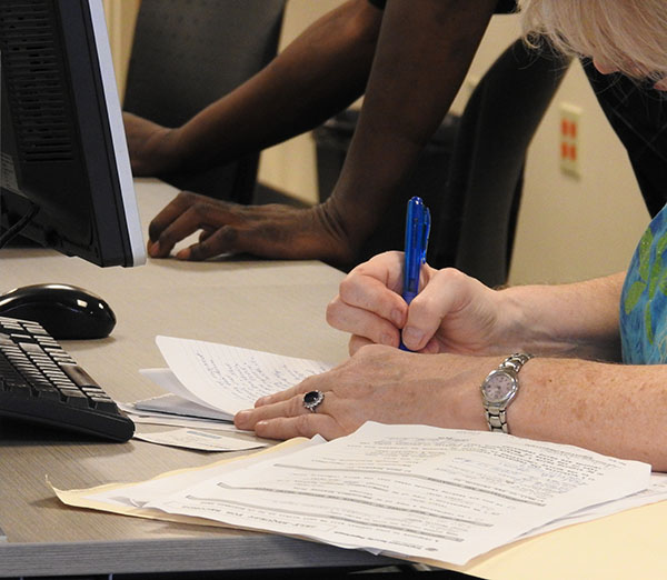 Woman's hands sign papers. She wears a wedding ring and watch.